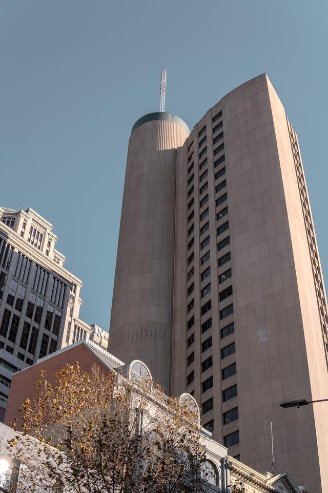 A tall cylindrical tower flanked by rectangular buildings against a clear blue sky