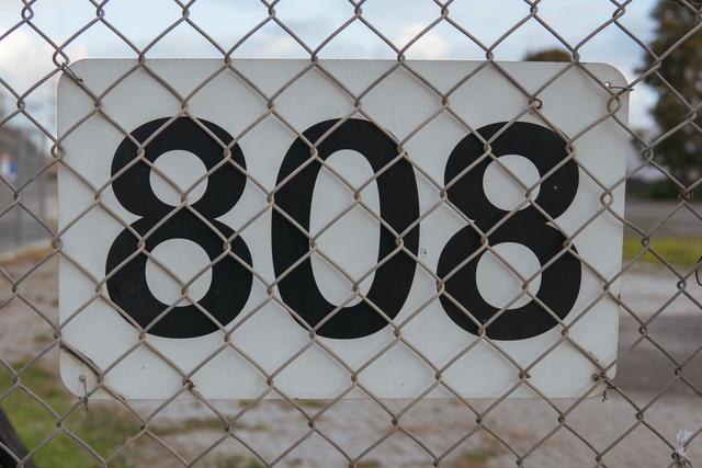 A chain-link fence in the foreground with a blurred background, and a white sign with the number 808 in bold black font visible through the fence