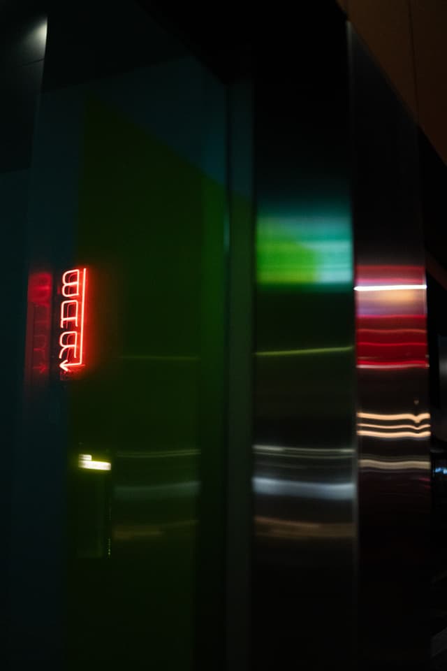 A dark scene with colorful light streaks, possibly from a moving vehicle or lights, with a red digital clock display reading 00:00 visible in the background