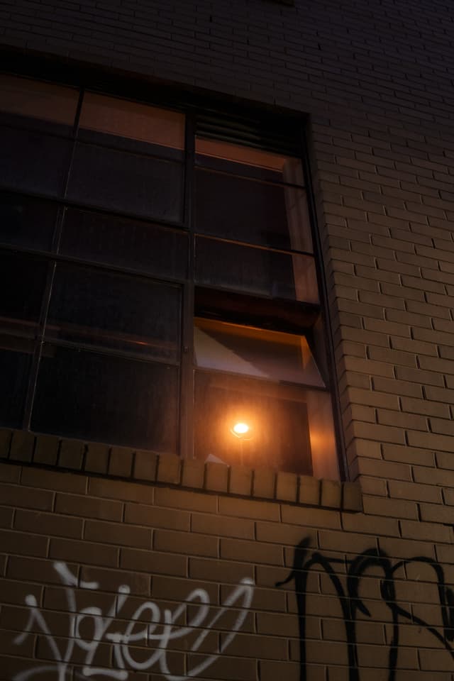 A dimly lit window on a brick wall with graffiti at night