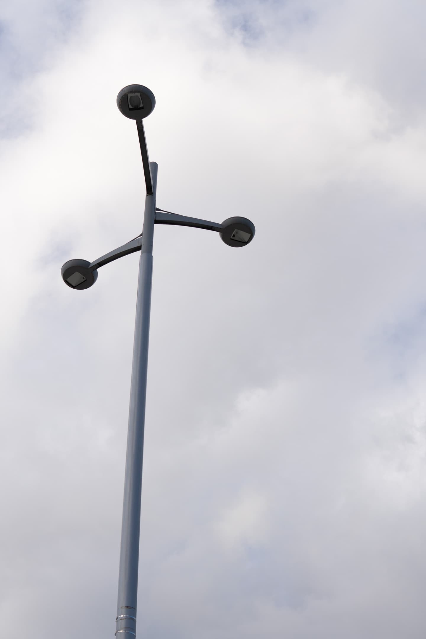 A street lamp with three globular fixtures extends into a cloudy sky