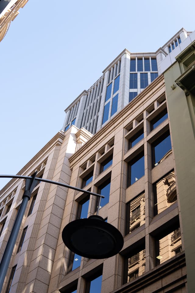 A view looking up at modern high-rise buildings against a clear blue sky, with a street lamp in the foreground