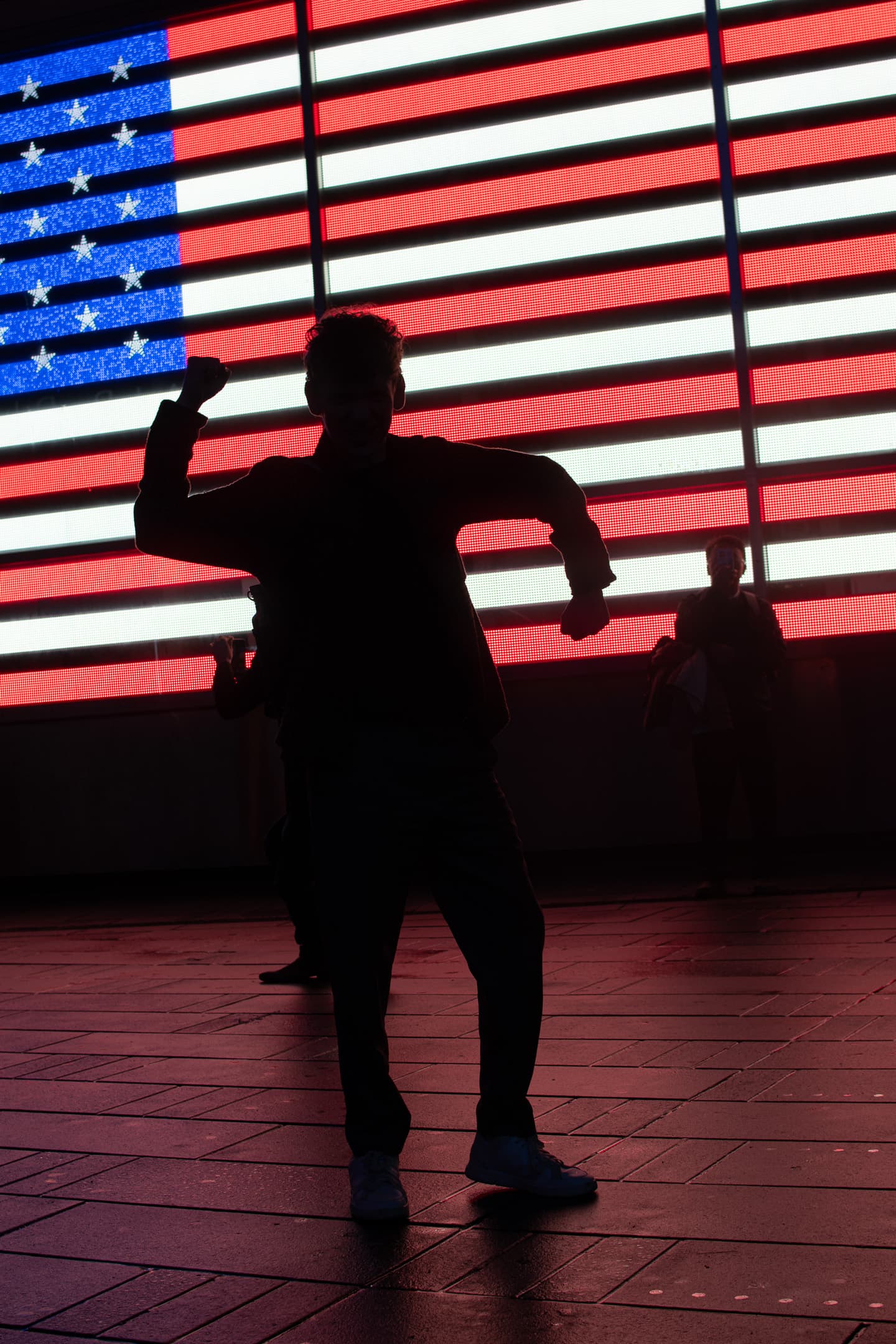 A silhouette of a person posing with an illuminated American flag in the background