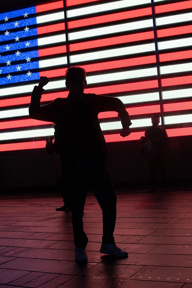 A silhouette of a person posing with an illuminated American flag in the background