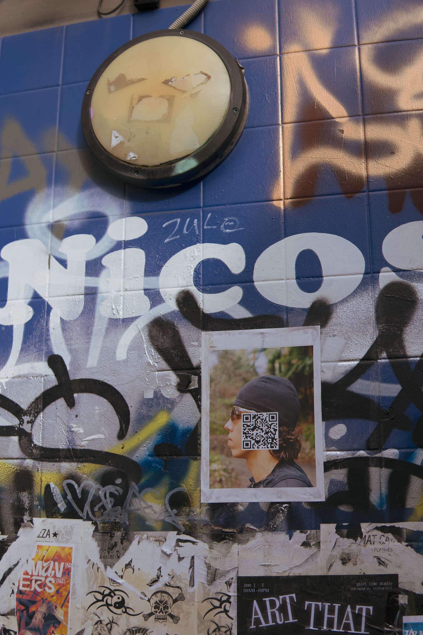 A wall covered in graffiti, posters, and a clock with its hands forming a sad face