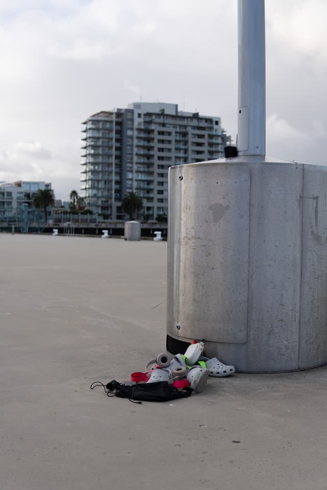 A collection of discarded items, including shoes and a bag, lies on the ground next to a concrete pillar with a cityscape in the background