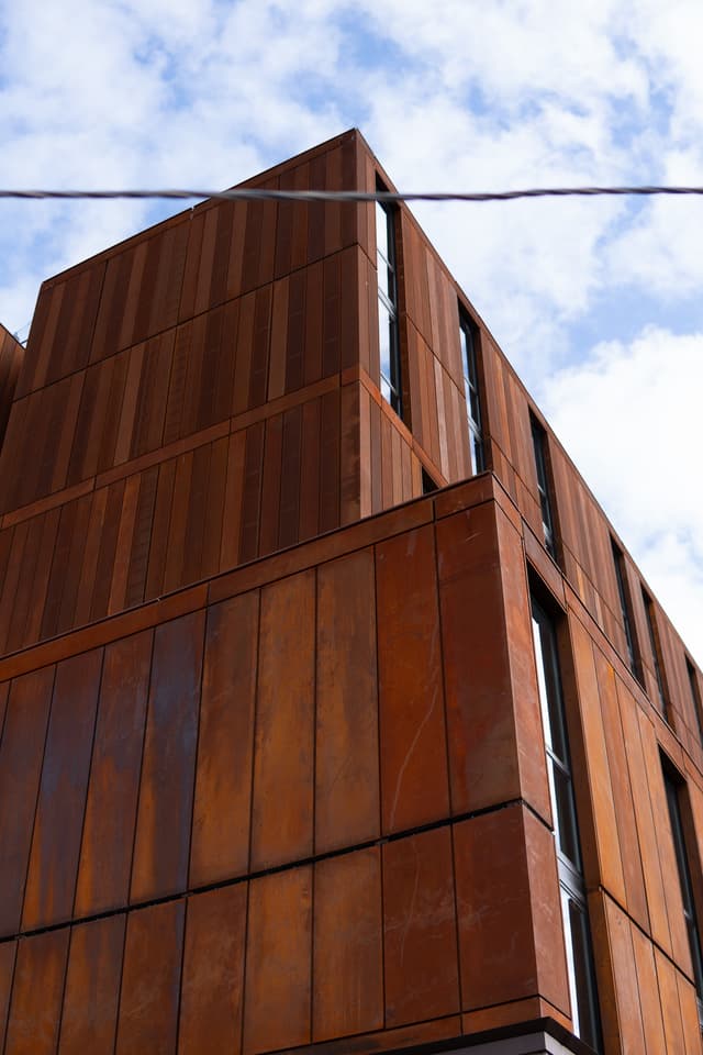 A modern building with rust-colored cladding and geometric design against a blue sky with clouds