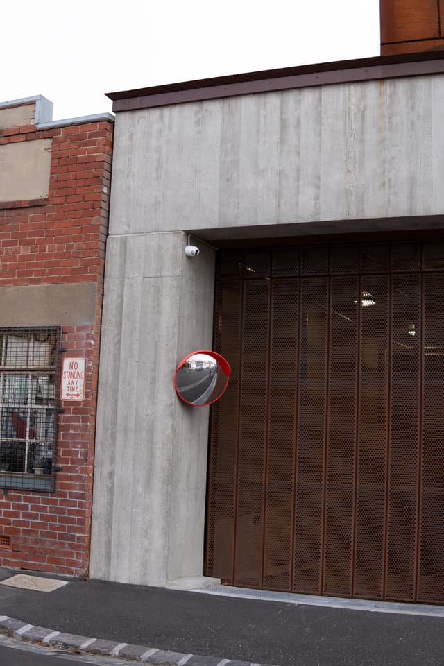 A convex traffic mirror is mounted on a concrete wall next to a wooden garage door, providing visibility for vehicles at a street corner