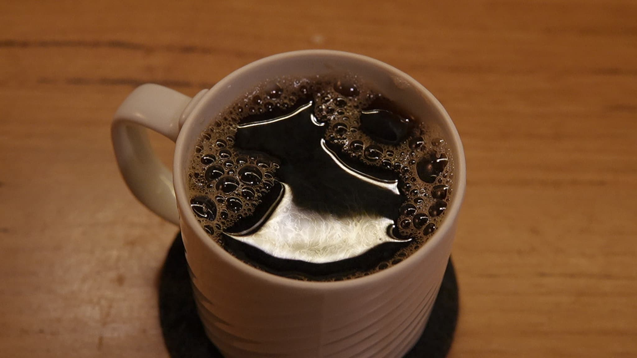 A white mug filled with a dark liquid, possibly coffee, on a wooden surface with a coaster underneath